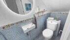 Modernes Badezimmer mit blauem Mosaikfliesenspiegel, buntem Fliesenbordüre, Wandwaschbecken und WC im Stadthaus Felanitx
