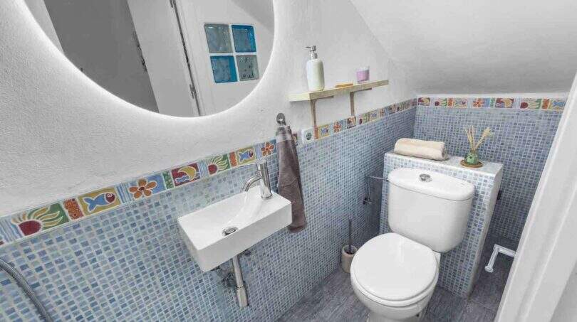 Modernes Badezimmer mit blauem Mosaikfliesenspiegel, buntem Fliesenbordüre, Wandwaschbecken und WC im Stadthaus Felanitx