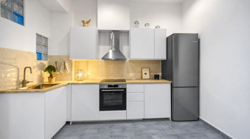 Moderne weiße Küche mit Holzarbeitsplatte, Einbauofen, Edelstahlkühlschrank und Glasbausteinfen in Felanitx