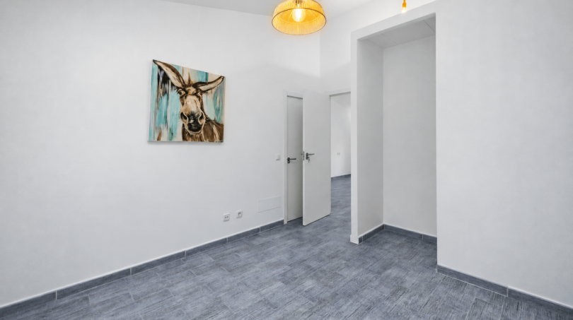 Helles, leeres Zimmer mit Granitboden, weißen Wänden, Pendelleuchte und Esel-Kunstwerk in modernem Stadthaus Felanitx