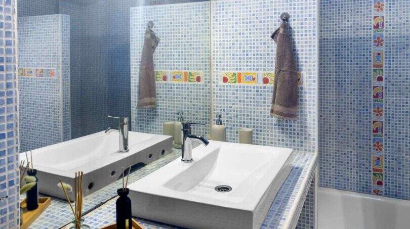 Modernes Badezimmer mit blauem Mosaikfliesenspiegel, zwei Aufsatzwaschbecken und bunten Akzentfliesen im Stadthaus Felanitx
