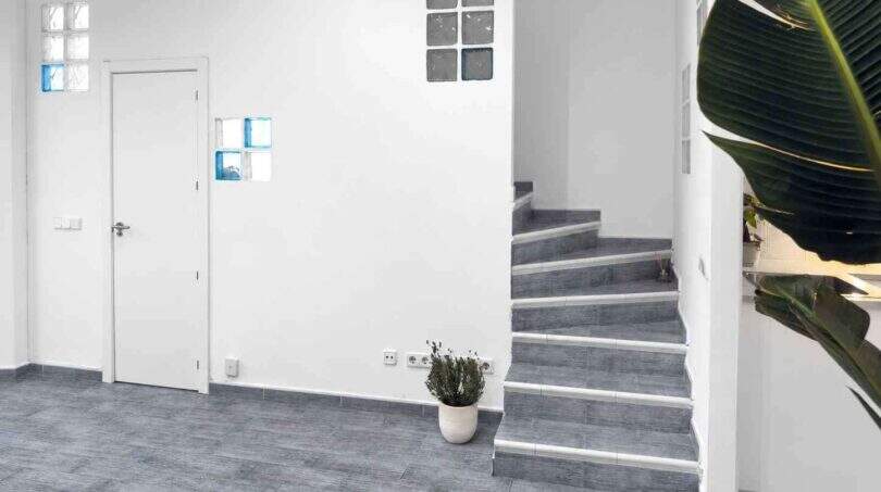 Helles Eingangsfoyer mit grauer Fliesenstätte, moderner Treppe, Glasbausteinakzenten und tropischer Pflanzendeko in Felanitx
