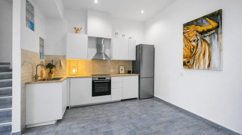 Moderne weiße Küche mit Holzarbeitsplatte, Edelstahlkühlschrank und Stiergemälde im Stadthaus Felanitx