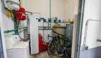 Utility room with washing machine, heating system, green pipes and bicycles in house in Felanitx