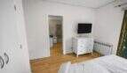 Bright bedroom with white dresser, wall TV, radiator and wooden floor in house in Felanitx