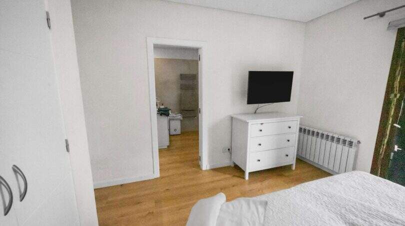 Bright bedroom with white dresser, wall TV, radiator and wooden floor in house in Felanitx