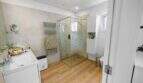 Modern bathroom with glass shower, wooden floor, towel radiator and white built-in furniture in house Felanitx