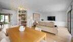 Bright living and dining room with wooden table, designer lamp, sofa group and TV area in house in Felanitx