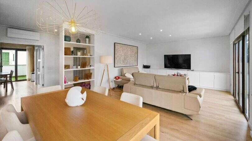 Bright living and dining room with wooden table, designer lamp, sofa group and TV area in house in Felanitx
