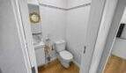 Small white guest toilet with hand wash basin, golden round mirror and wooden floor in the house in Felanitx