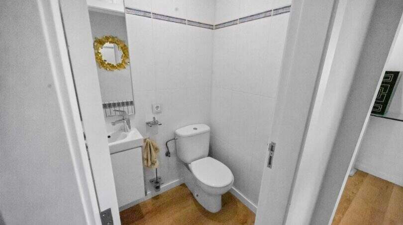 Small white guest toilet with hand wash basin, golden round mirror and wooden floor in the house in Felanitx
