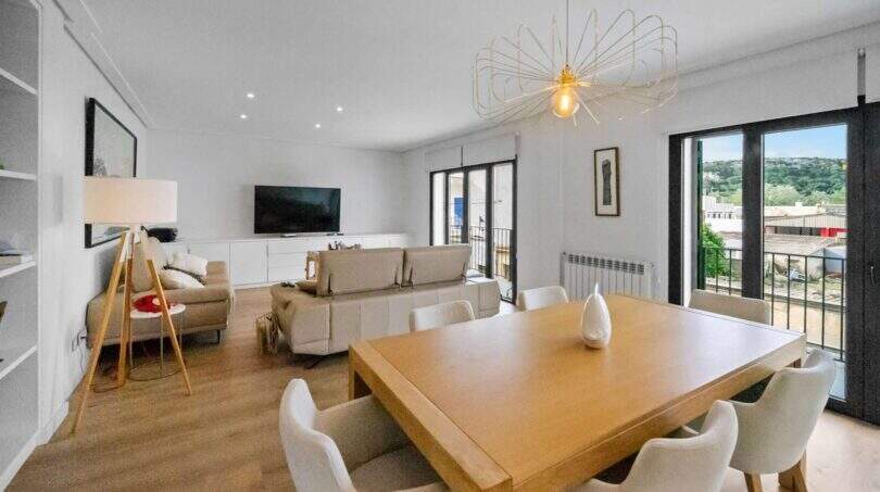 Bright living-dining room with wooden table, white chairs, sofa and balcony access in house in Felanitx