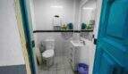 Small, white-tiled bathroom with toilet, sink, mirror and blue door in house in Felanitx.