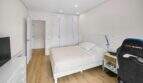 Bright bedroom with double bed, white built-in wardrobe, wooden floor and gaming chair in house Felanitx