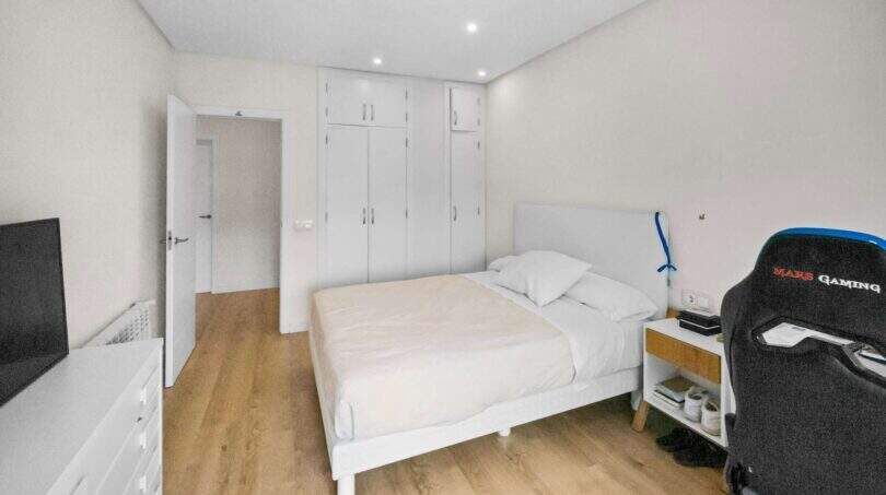 Bright bedroom with double bed, white built-in wardrobe, wooden floor and gaming chair in house Felanitx