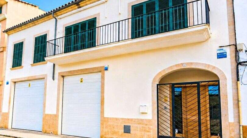 Exterior view of a white house in Felanitx with double garage, balcony and green shutters.