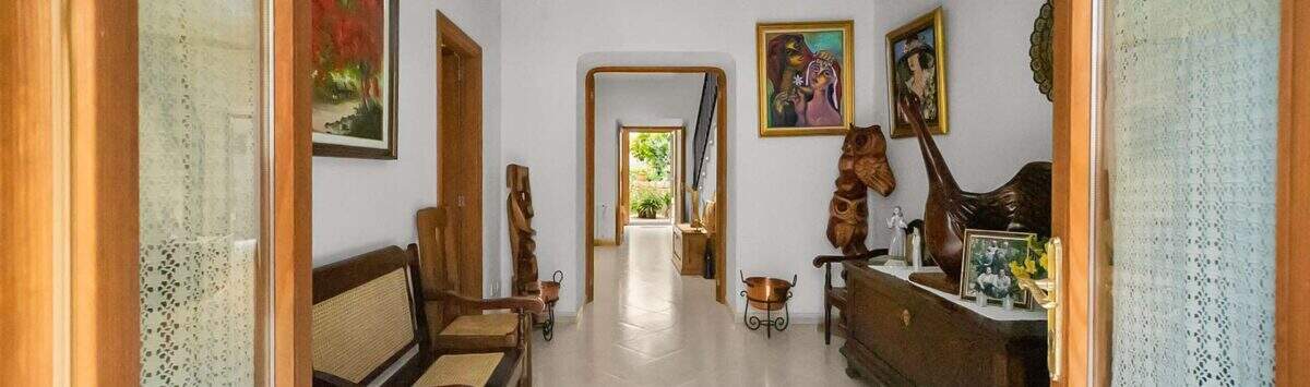 Entrance hall of the townhouse with wooden beam ceiling, rattan furniture, paintings and rustic wooden sculptures in Felanitx.