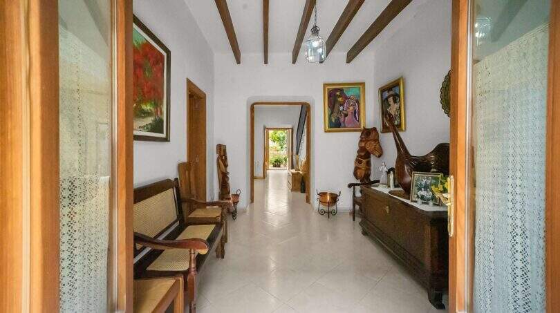 Entrance hall of the townhouse with wooden beam ceiling, rattan furniture, paintings and rustic wooden sculptures in Felanitx.