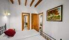 Bedroom with wooden beam ceiling, wrought iron bed, two doors and painting in the Felanitx town house