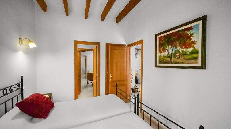 Bedroom with wooden beam ceiling, wrought iron bed, two doors and painting in the Felanitx town house