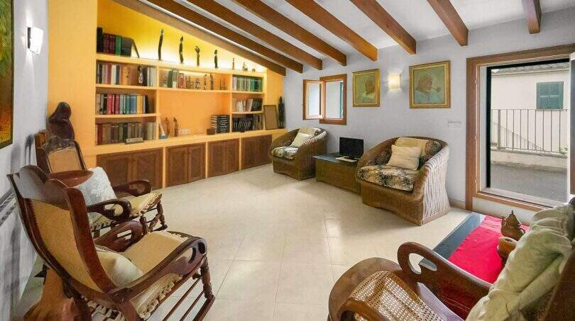 Living room with wooden beam ceiling, illuminated library and rattan furniture in the Felanitx townhouse