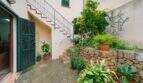 Courtyard of the townhouse in Felanitx with stone wall, lush plants, external staircase and green wooden shutters.
