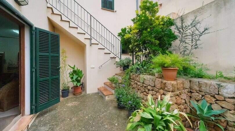 Courtyard of the townhouse in Felanitx with stone wall, lush plants, external staircase and green wooden shutters.