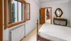 Bright bedroom with wooden bed, antique console table, mirror, radiator and shutters in the Felanitx town house.
