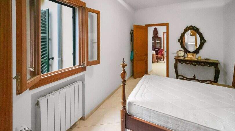 Bright bedroom with wooden bed, antique console table, mirror, radiator and shutters in the Felanitx town house.