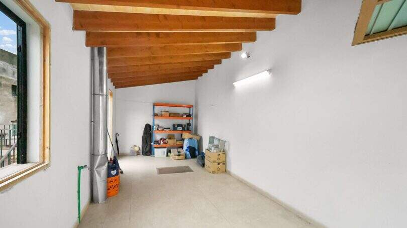 Storage room with wooden beam ceiling, metal pipe, shelves and cardboard boxes in the 1900 townhouse in Felanitx.