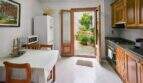 Bright kitchen with wooden furniture, dining table and open door to the green courtyard of the townhouse in Felanitx.