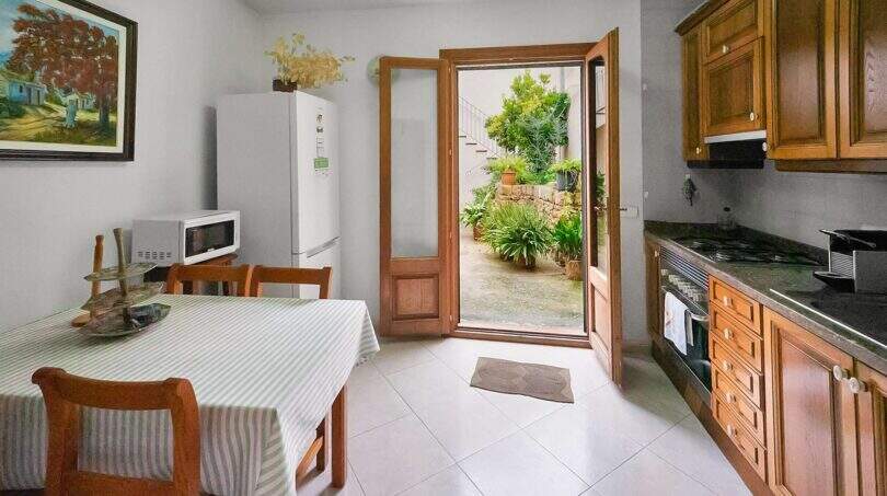 Bright kitchen with wooden furniture, dining table and open door to the green courtyard of the townhouse in Felanitx.