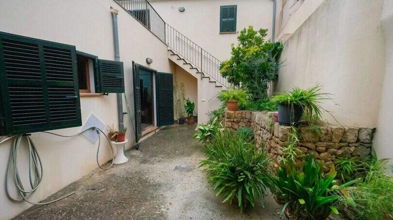 Courtyard of the historic townhouse in Felanitx with external staircase, green shutters and lush vegetation.