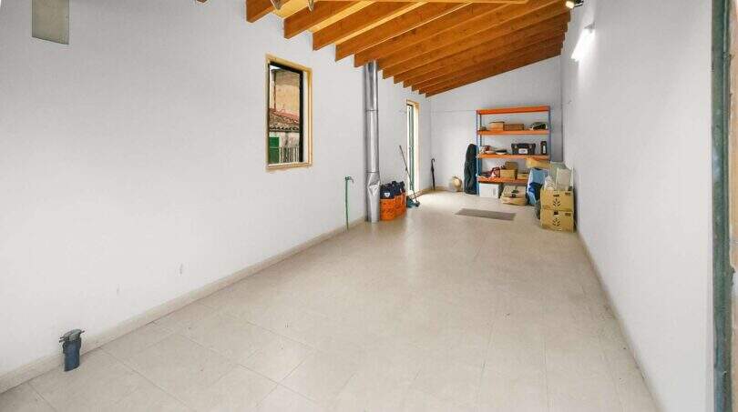 Spacious garage with wooden beam ceiling, shelf space and bright tiled floor in the Felanitx townhouse