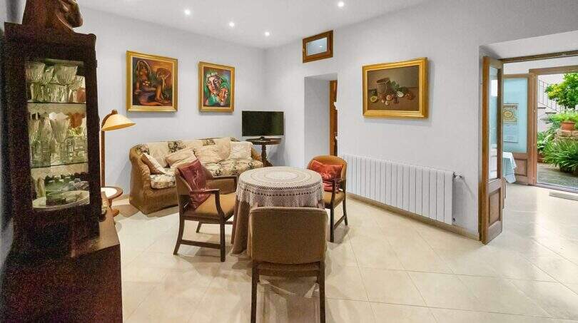 Living room with sofa, paintings, display cabinet and terracotta floor in the 1900 town house in Felanitx