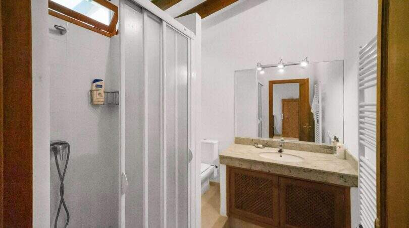Bathroom with shower cubicle, marble washbasin, wooden base cabinet and towel heater in the Felanitx townhouse
