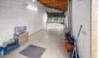 Narrow garage with wooden beam ceiling, open roller door, gas bottles and cardboard boxes in Felanitx