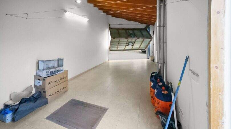 Narrow garage with wooden beam ceiling, open roller door, gas bottles and cardboard boxes in Felanitx