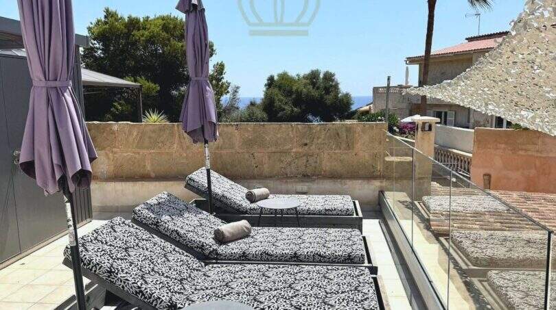 Dachterrasse mit Sonnenliegen und lila Sonnenschirmen, Glasgeländer und Meerblick in Cala Llombards