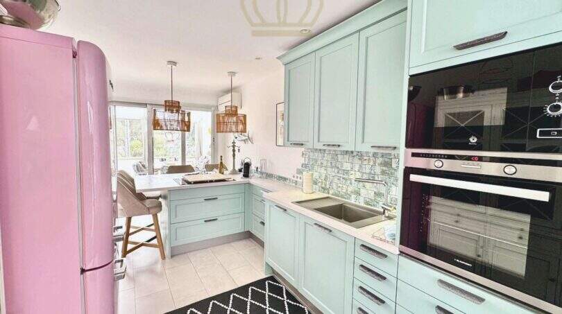 Moderne Küche mit mintgrünen Schränken, rosa Retro-Kühlschrank und Essbereich in Cala Llombards