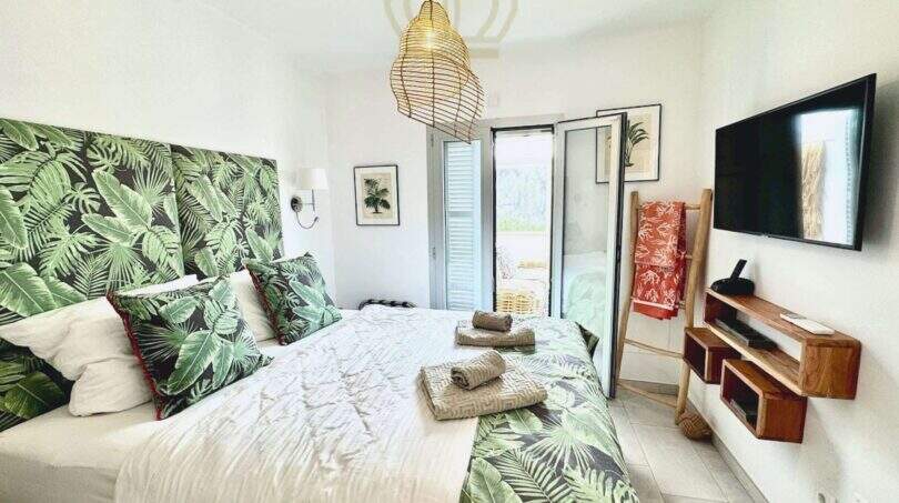 Tropisch gestaltetes Schlafzimmer mit Doppelbett, Palmenmuster-Kopfteil, TV und Balkonzugang in Cala Llombards