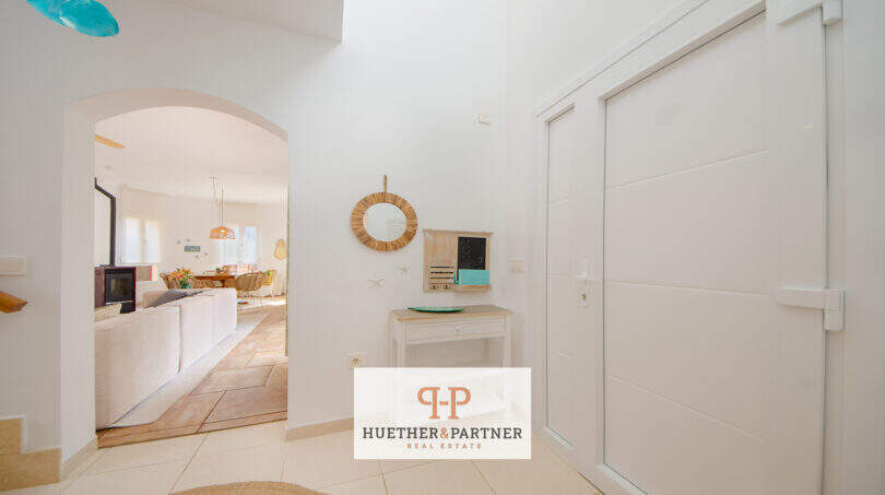 Heller Eingangsbereich mit weißer Tür, Rundspiegel und Blick ins Wohnzimmer mit Kamin, Haus in Cala Murada