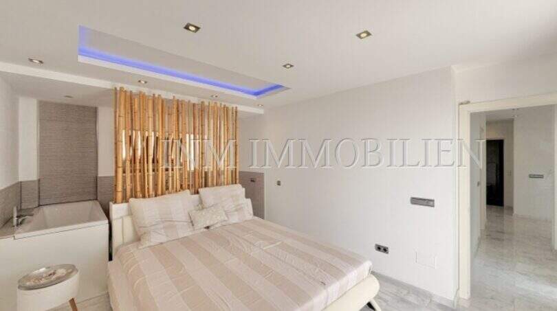 Helles Schlafzimmer im Penthouse Cala Pi mit Doppelbett, Bambus-Raumteiler, Badewanne und LED-Deckenbeleuchtung.