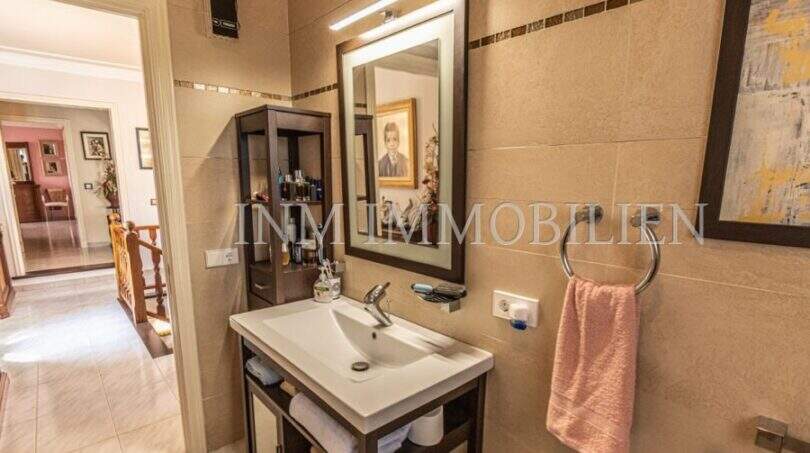 Modernes Badezimmer der Villa in Marratxí mit elegantem Waschtisch, beleuchtetem Spiegel und Beige-Fliesen.