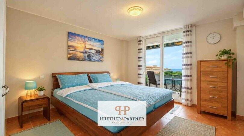 Helles Schlafzimmer mit Doppelbett, Holzmöbeln und Balkon mit Meerblick in der Wohnung in Cales de Mallorca.