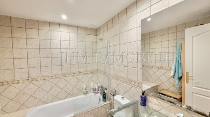 Helles Badezimmer mit Einbaubadewanne, beigen Fliesen und Waschtisch im Reiheneckhaus in Pollença.