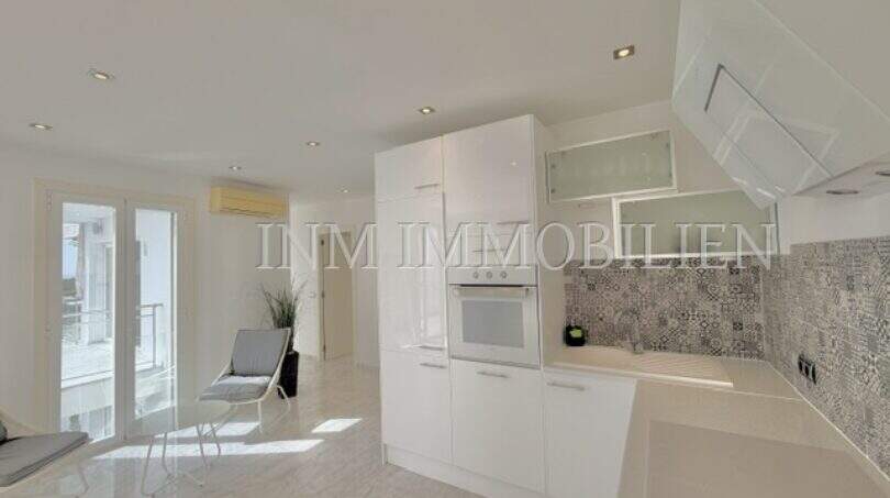 Moderne weiße Küche mit Backofen, Musterfliesenspiegel und offenem Wohnbereich mit Terrassenzugang im Penthouse Cala Pi.