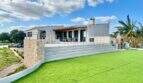 Exterior view Campos finca: modern country house with extensive lawn, terrace, stone wall and palm tree under blue sky.