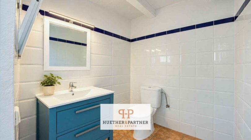 Baño luminoso de la finca en Felanitx con lavamanos azul, azulejos blancos y patrón de cenefa azul.