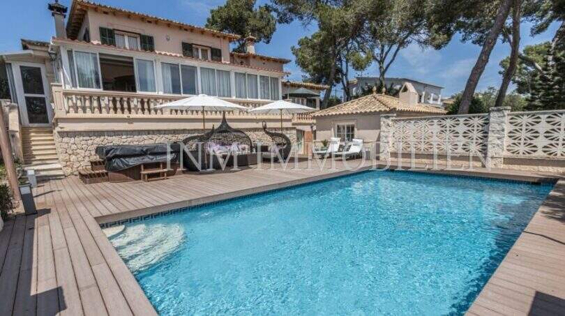 Villa in Marratxí: Außenbereich mit blauem Pool, Holzterrasse, Sonnenliegen und mediterraner Fassade mit Pinien.